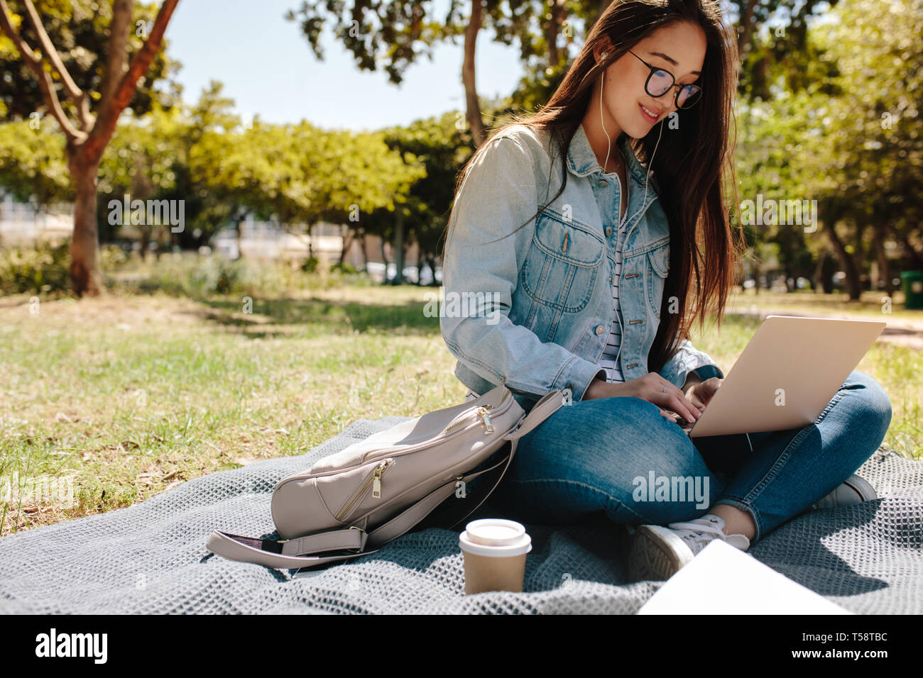 Sorridente collegio asiatico ragazza utilizzando un computer portatile in seduta il college campus in una giornata di sole. Ragazza giovane facendo il suo lavoro college sul laptop o di seduta Foto Stock