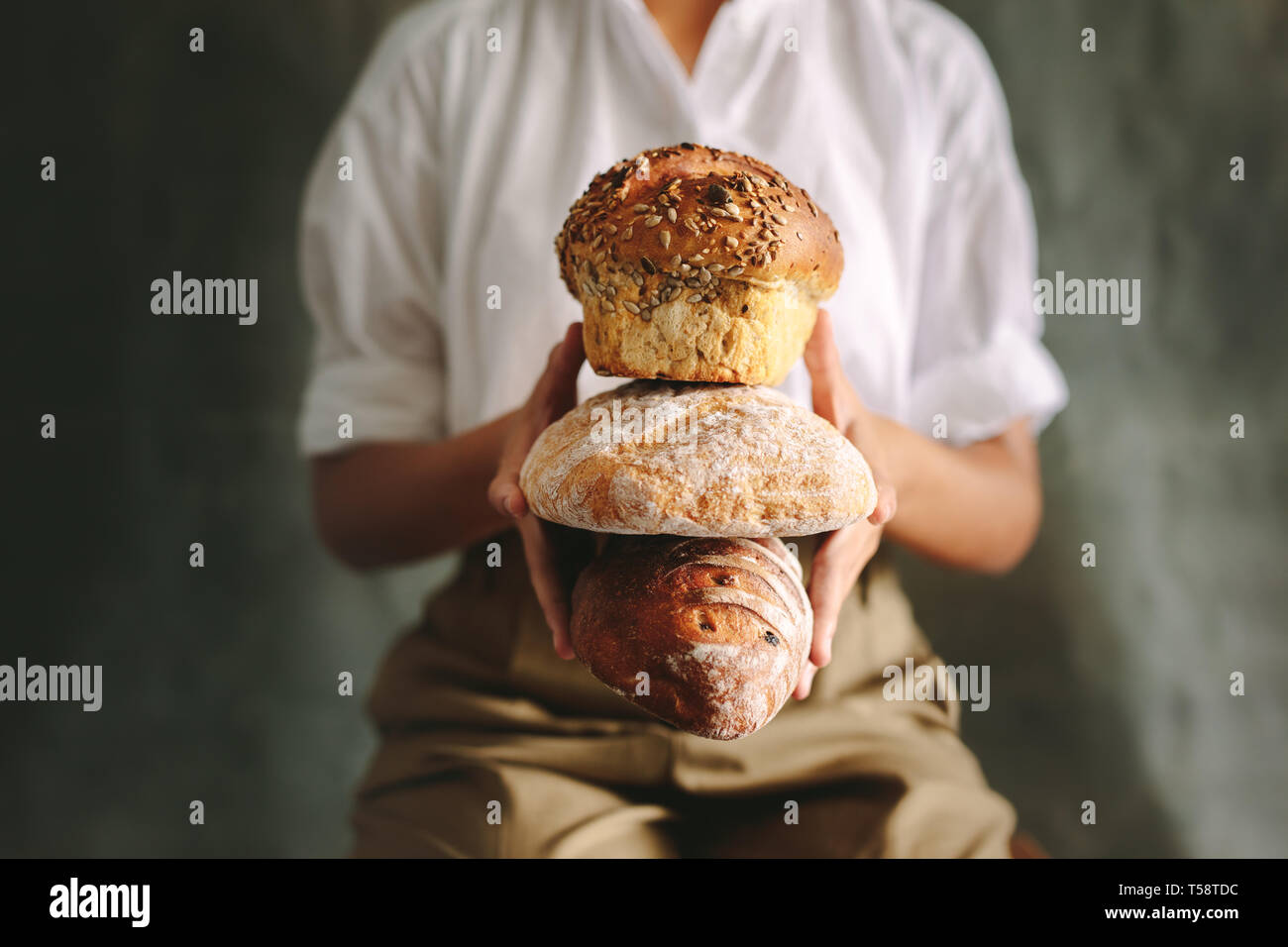 Close up baker femmina holding di diversi tipi di pane. Lo Chef holding di vari tipi di pane contro uno sfondo grigio. Foto Stock