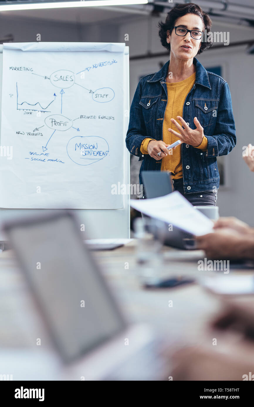 Donna caucasica che parla con i colleghi durante la presentazione aziendale. donna d'affari che condivide la sua strategia con il team nella sala conferenze. Foto Stock