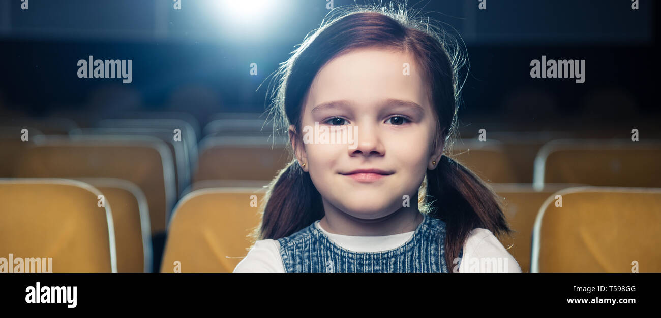 Panoramica della cute brunette bambino seduto in cinema e guardando la fotocamera Foto Stock