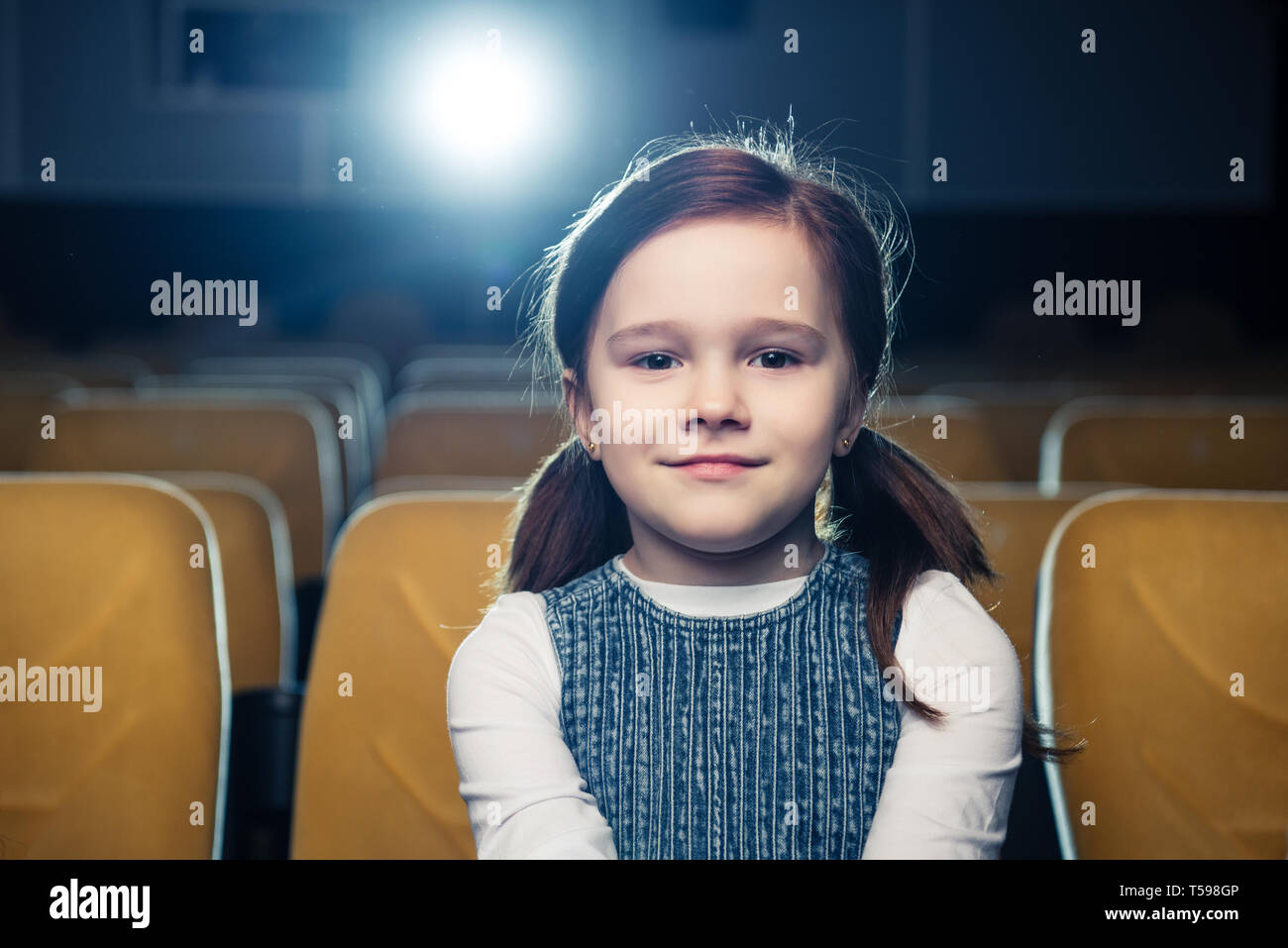 Carino brunette bambino seduto in cinema e guardando la fotocamera Foto Stock