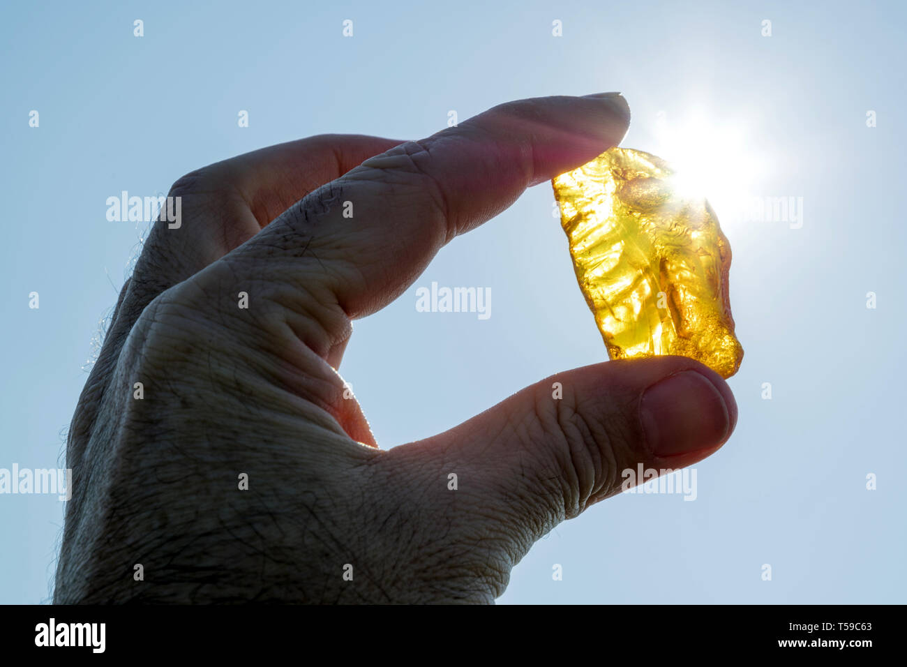 Maschio di mano trattiene ambra contro il sole Foto Stock