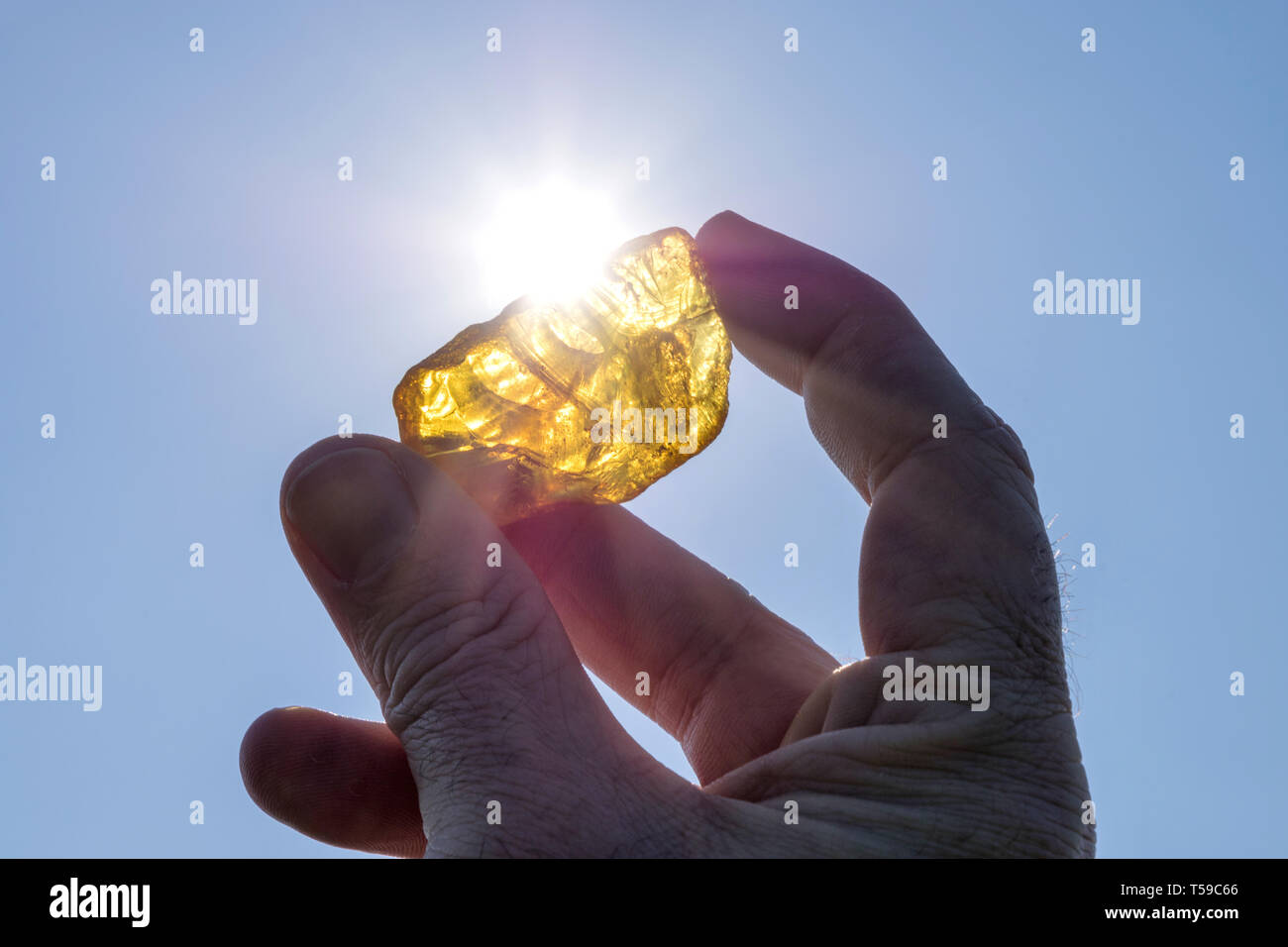 Maschio di mano trattiene ambra contro il sole Foto Stock