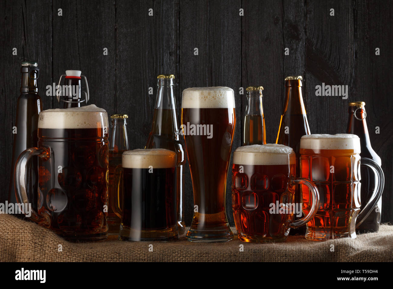 Bicchieri e bottiglie con lager, dark lager, brown ale, malto e birra Stout su tavola, scuro dello sfondo in legno Foto Stock