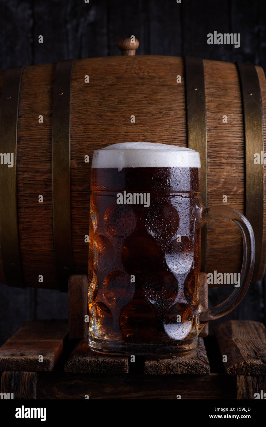 Grande boccale di birra sulla vecchia gabbia in legno con vintage barile di birra su sfondo scuro, still life Foto Stock