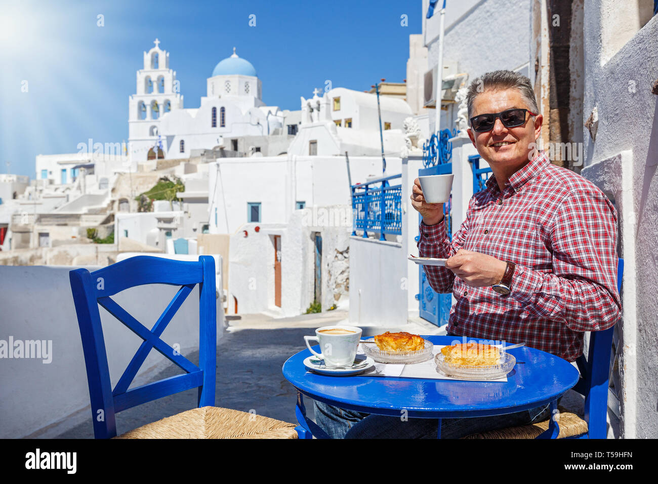 L uomo ha la colazione e le bevande di caffè in un bar per le strade di Santorini. Foto Stock