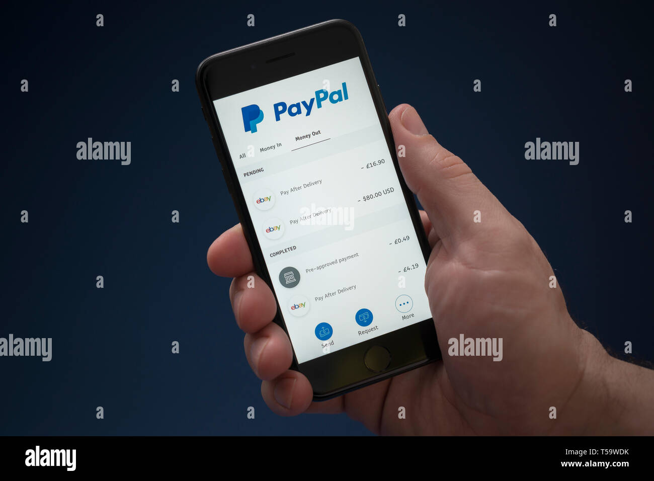 Un uomo guarda al suo iPhone che visualizza il logo di PayPal (solo uso editoriale). Foto Stock