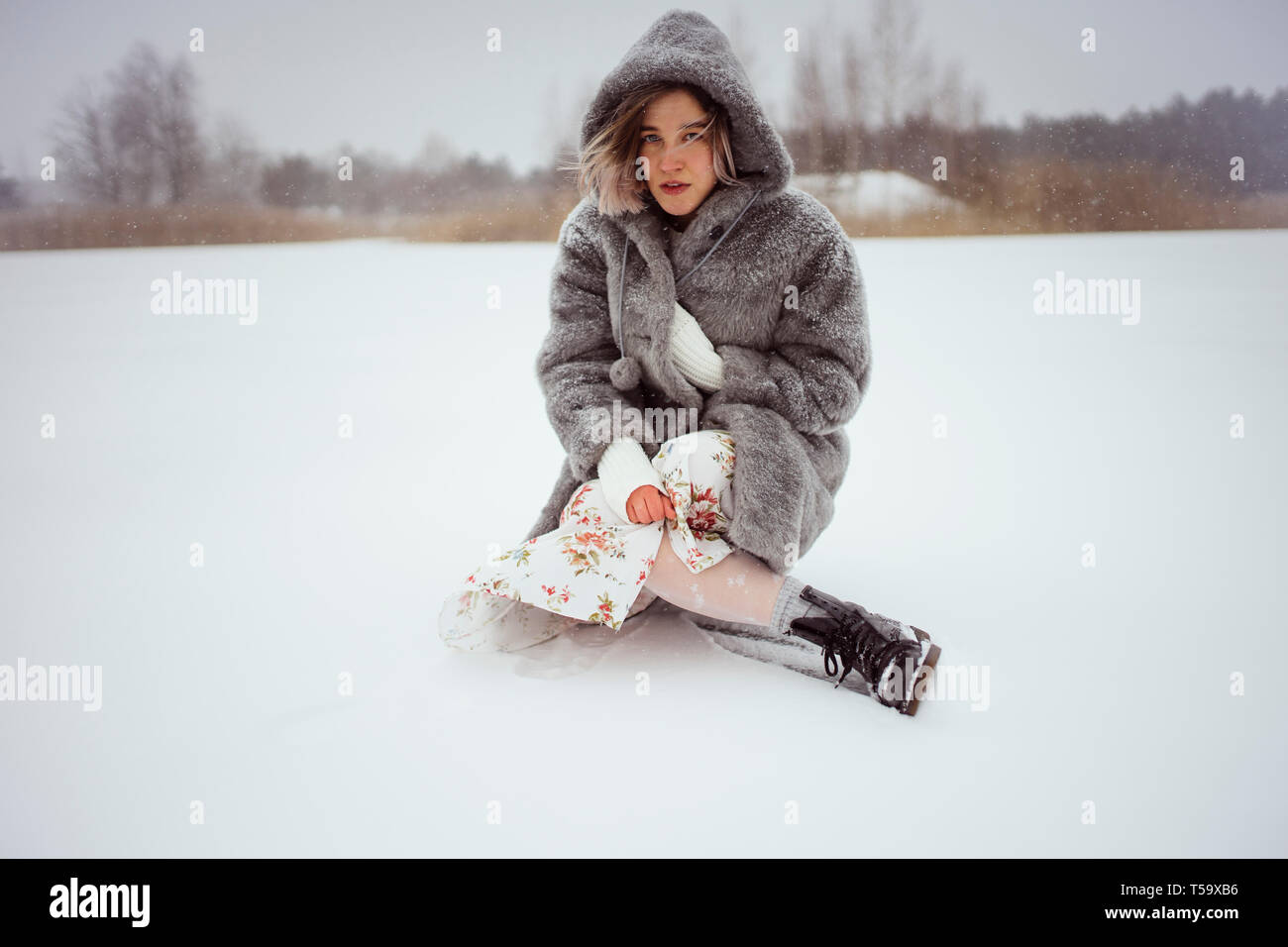 Una donna in pelliccia si siede su un lago innevato in inverno Foto Stock