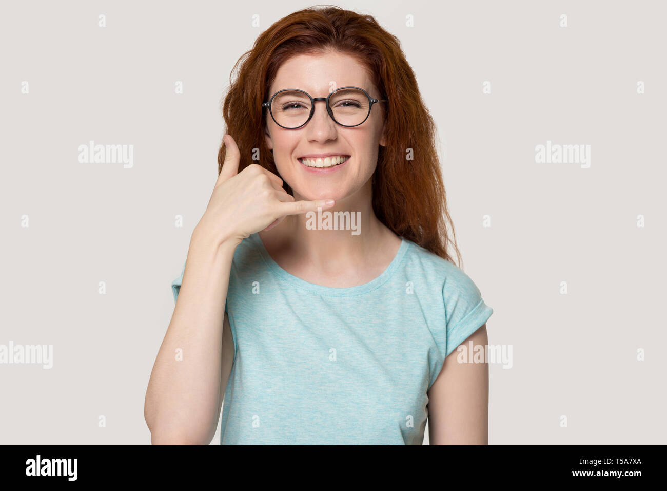 Redhead sorridente ragazza in bicchieri mostra chiamata gesto del telefono Foto Stock