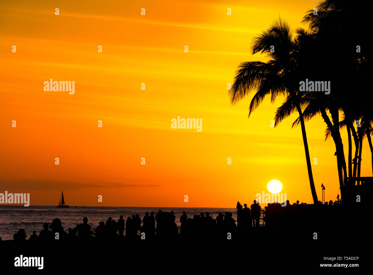 La folla di turisti si riuniscono per guardare un arancione tramonto sulla spiaggia di Waikiki di Oahu Honolulu Hawaii USA Foto Stock