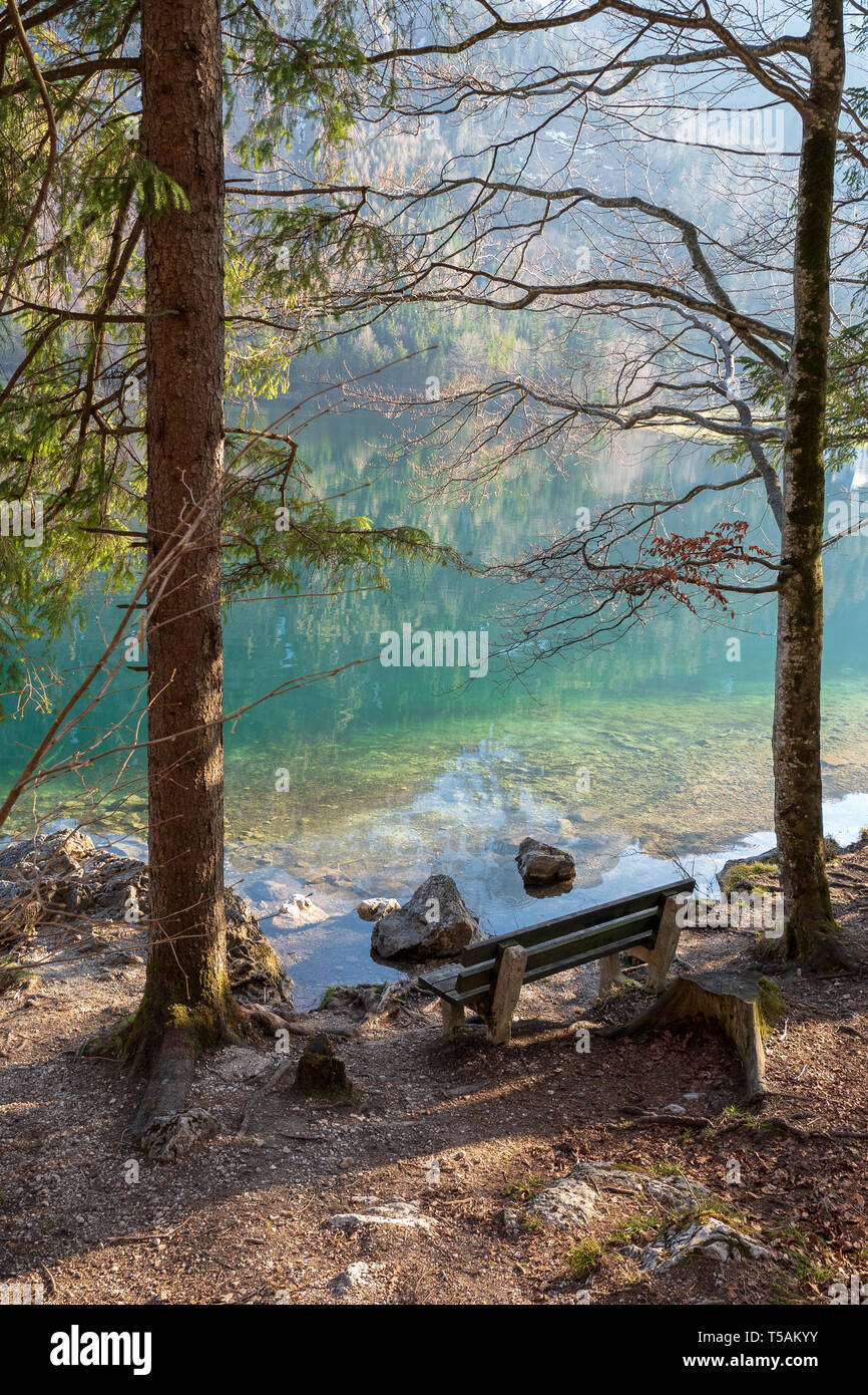 Svuotare panca in legno sulla riva della Vorderer Langbathsee vicino Ebensee, OÖ, Austria, con il grande paesaggio riflettendo sull'acqua cristallina Foto Stock
