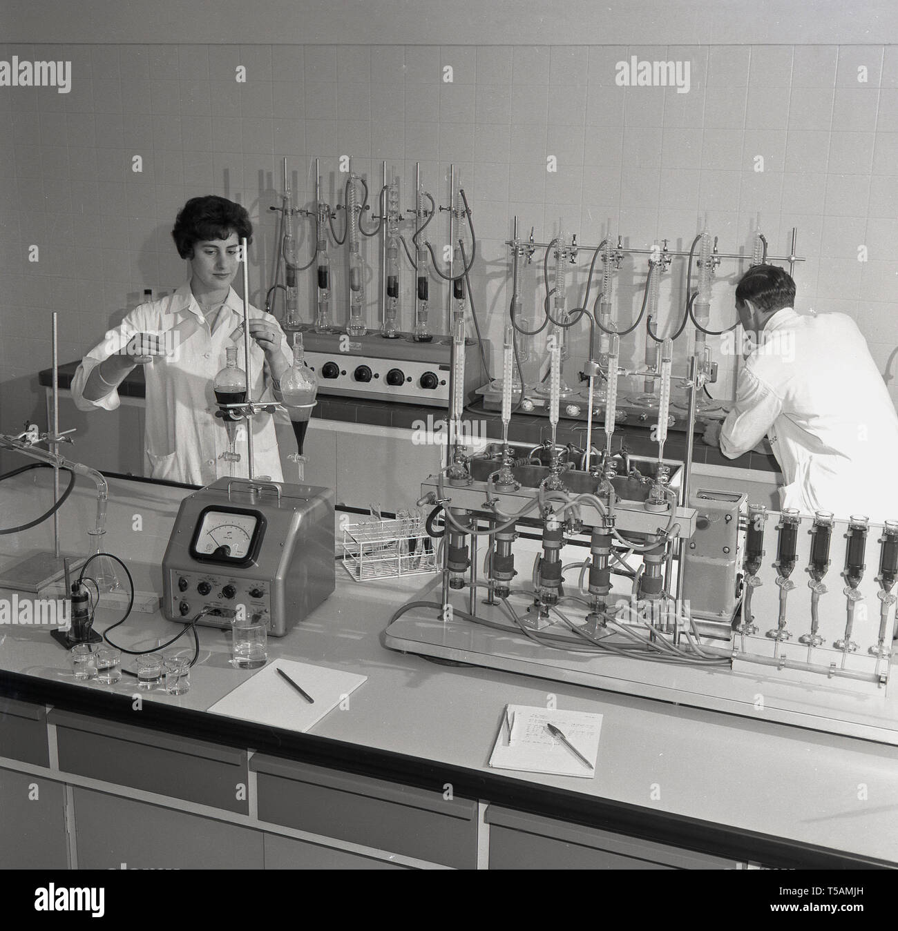 Anni '1950, storico, uno scienziato maschio e una giovane assistente di ricerca donna entrambi in camice bianco che intraprendono esperimenti con provette di prova e apparecchiature di misurazione in un laboratorio, in Inghilterra. Regno Unito, dove stanno studiando piante e orticoltura. Foto Stock
