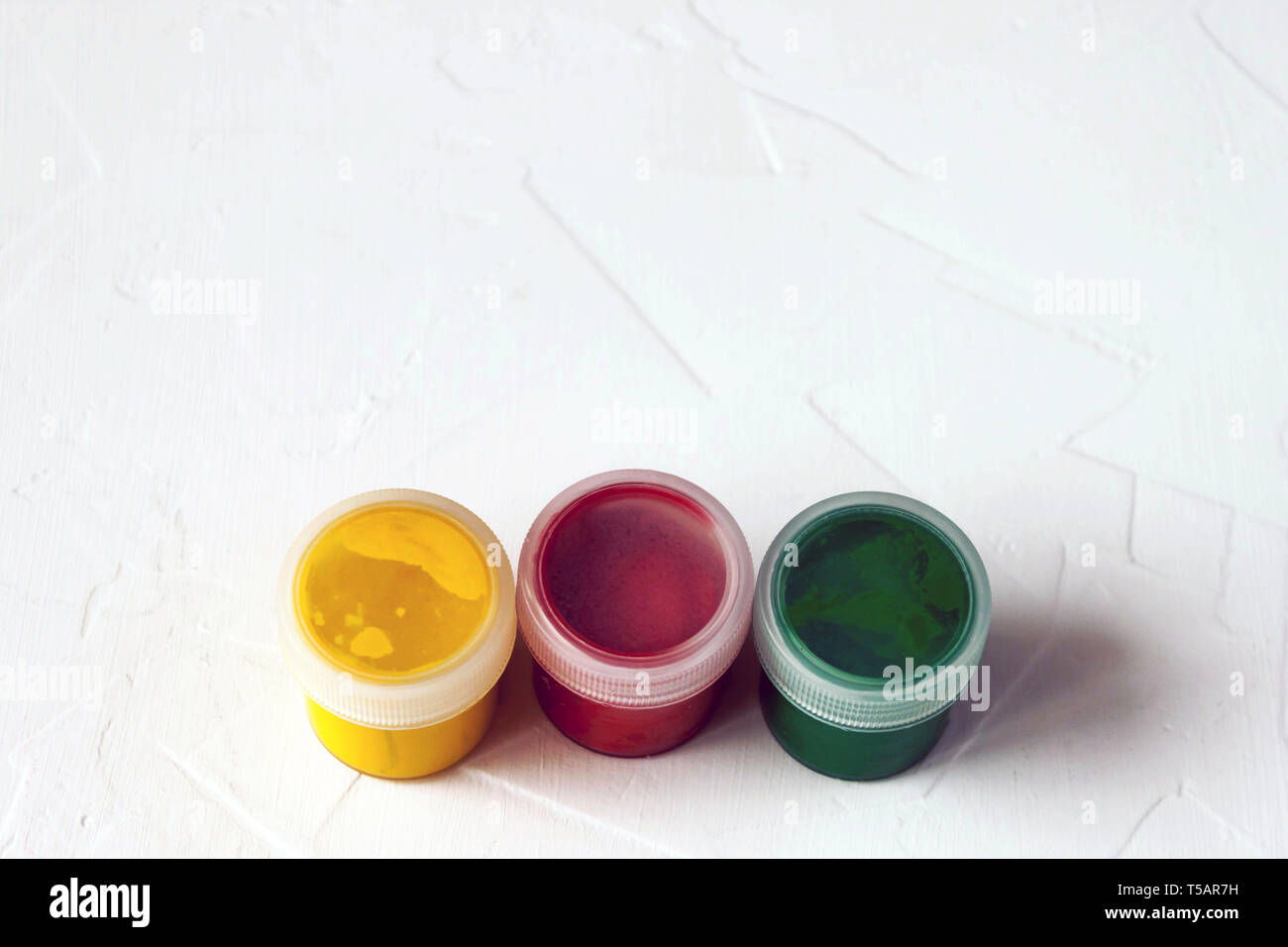 Tre vasetti di plastica con multy-gouache colorate o vernici acriliche tappo superiore vista su una luce sullo sfondo bianco. Soft selettiva fokus. Copia di testo spazio. Foto Stock
