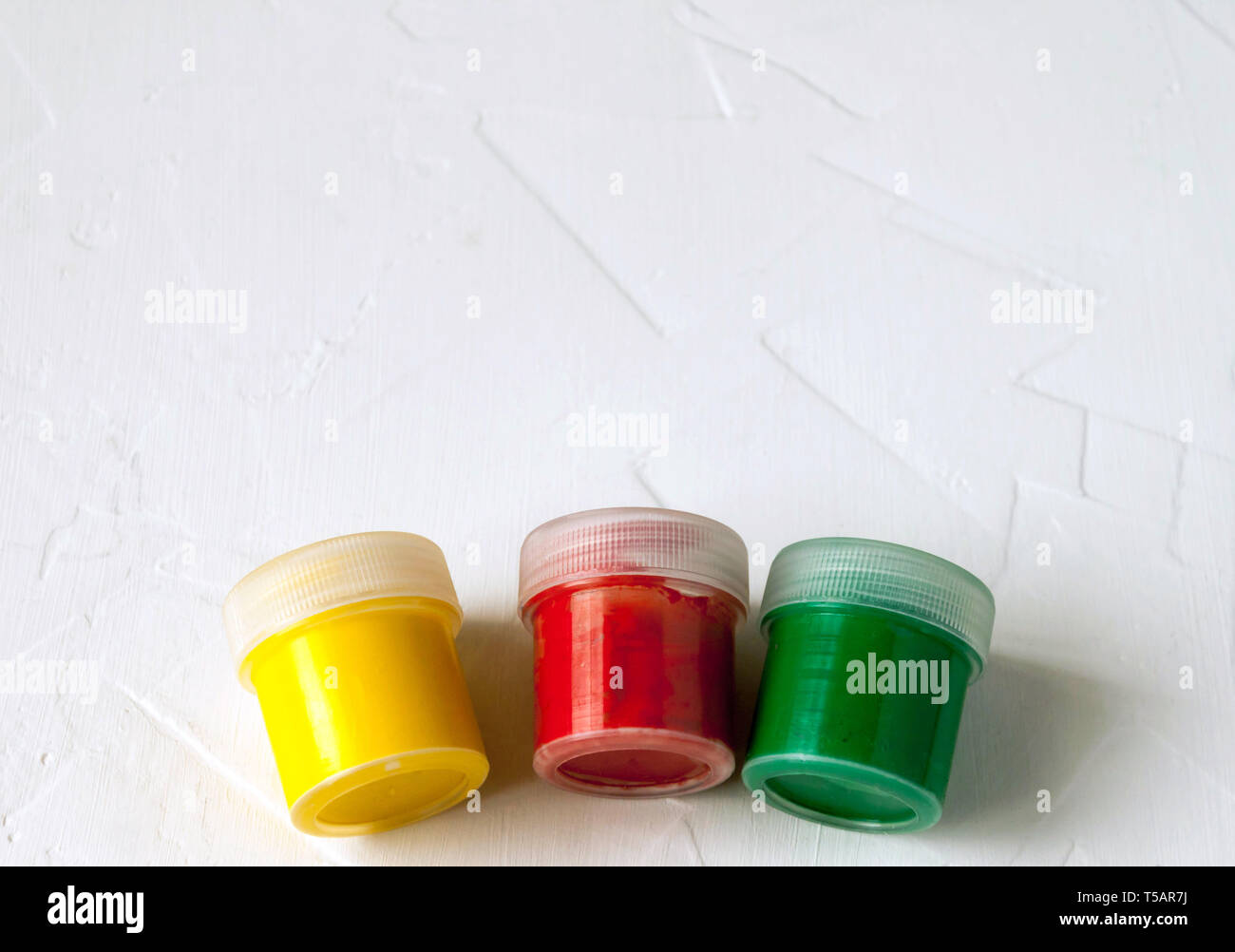 Tre vasetti di plastica con multy-gouache colorate o vernici acriliche vista laterale su una luce sullo sfondo bianco. Soft selettiva fokus. Copia di testo spazio. Foto Stock