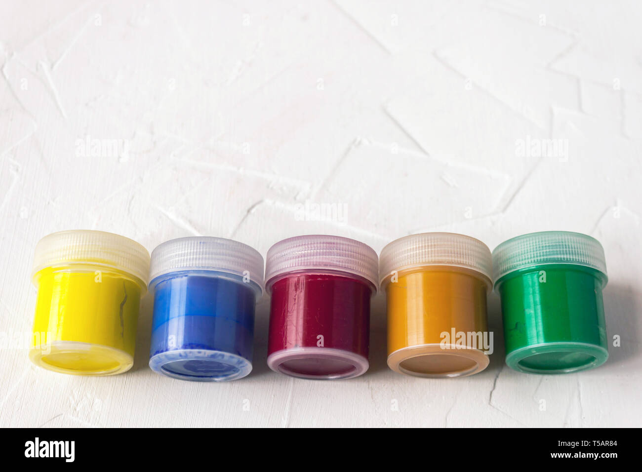 Cinque vasetti di plastica con multy-gouache colorate o acrilico vista superiore su una luce sullo sfondo bianco. Soft selettiva fokus. Copia di testo spazio. Foto Stock