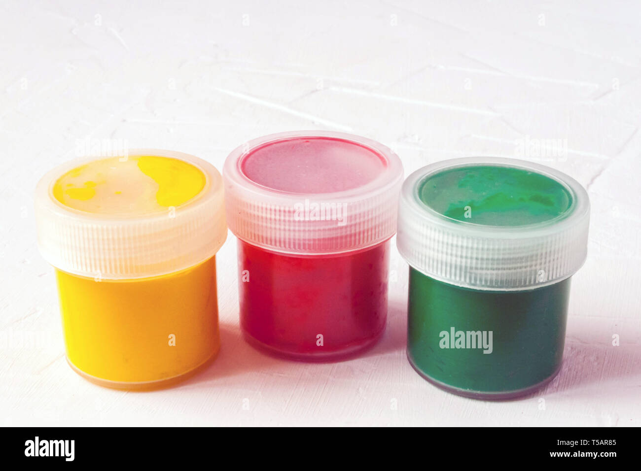 Tre vasetti di plastica con multy-gouache colorate o vernici acriliche vista laterale su una luce sullo sfondo bianco. Soft selettiva fokus. Copia di testo spazio. Foto Stock