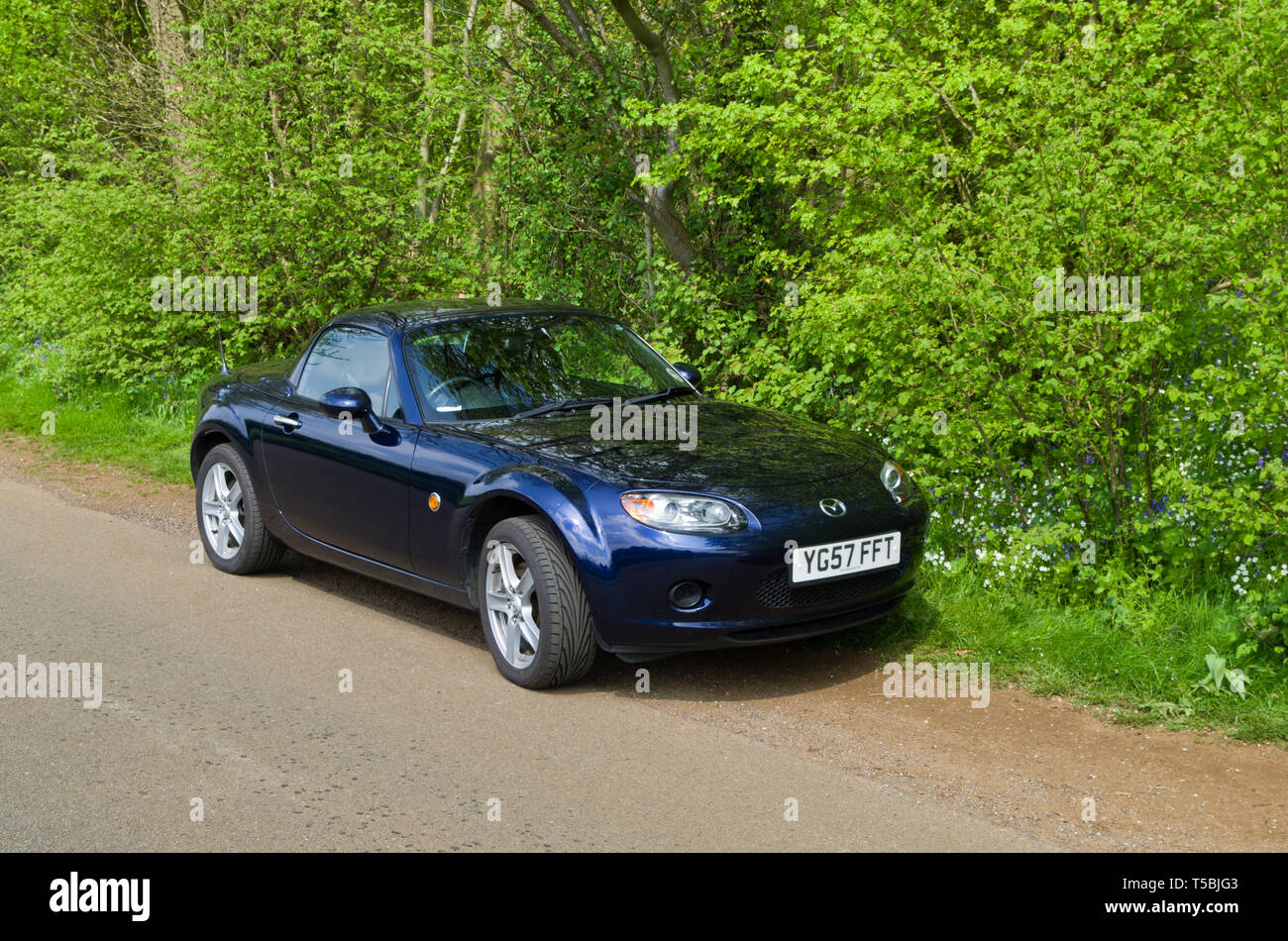 Mazda MX5 roadster parcheggiato contro lo sfondo di un bosco inglese in primavera. Foto Stock