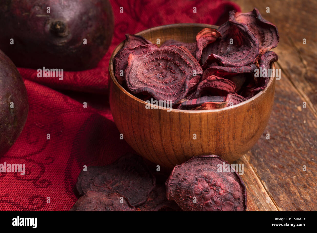 Close-up chips di barbabietole in ciotola di legno e tutta la barbabietole sul tovagliolo rosso sul vecchio tavolo in legno. Foto Stock Close-up chips di barbabietole in ciotola di legno e tutta la barbabietole sul tovagliolo rosso sul vecchio tavolo in legno. Foto Stock