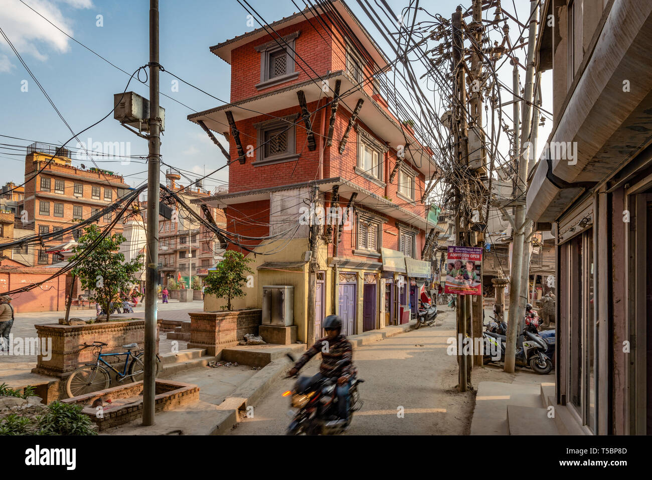 LALITPUR, PATAN NEPAL - Aprile 3, 2019: un motociclista sta andando giù per una strada stretta con un enorme numero di impianti elettrici e i cavi telefonici Foto Stock