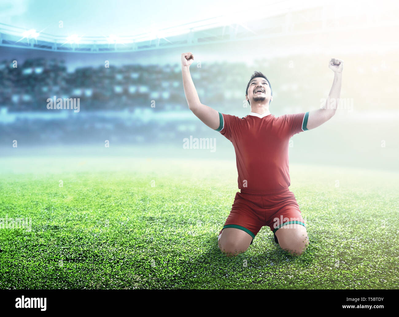 Giocatore di football uomo festeggiare il suo obiettivo con i bracci sollevati e in ginocchio sul campo di calcio a Stadium Foto Stock
