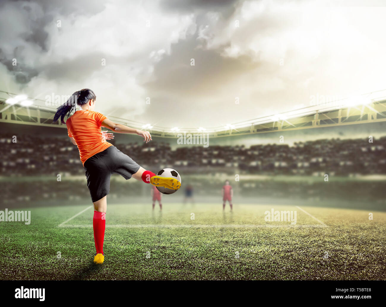 Vista posteriore di asian football player donna in maglia arancione calciare la palla sul campo di calcio a Stadium Foto Stock