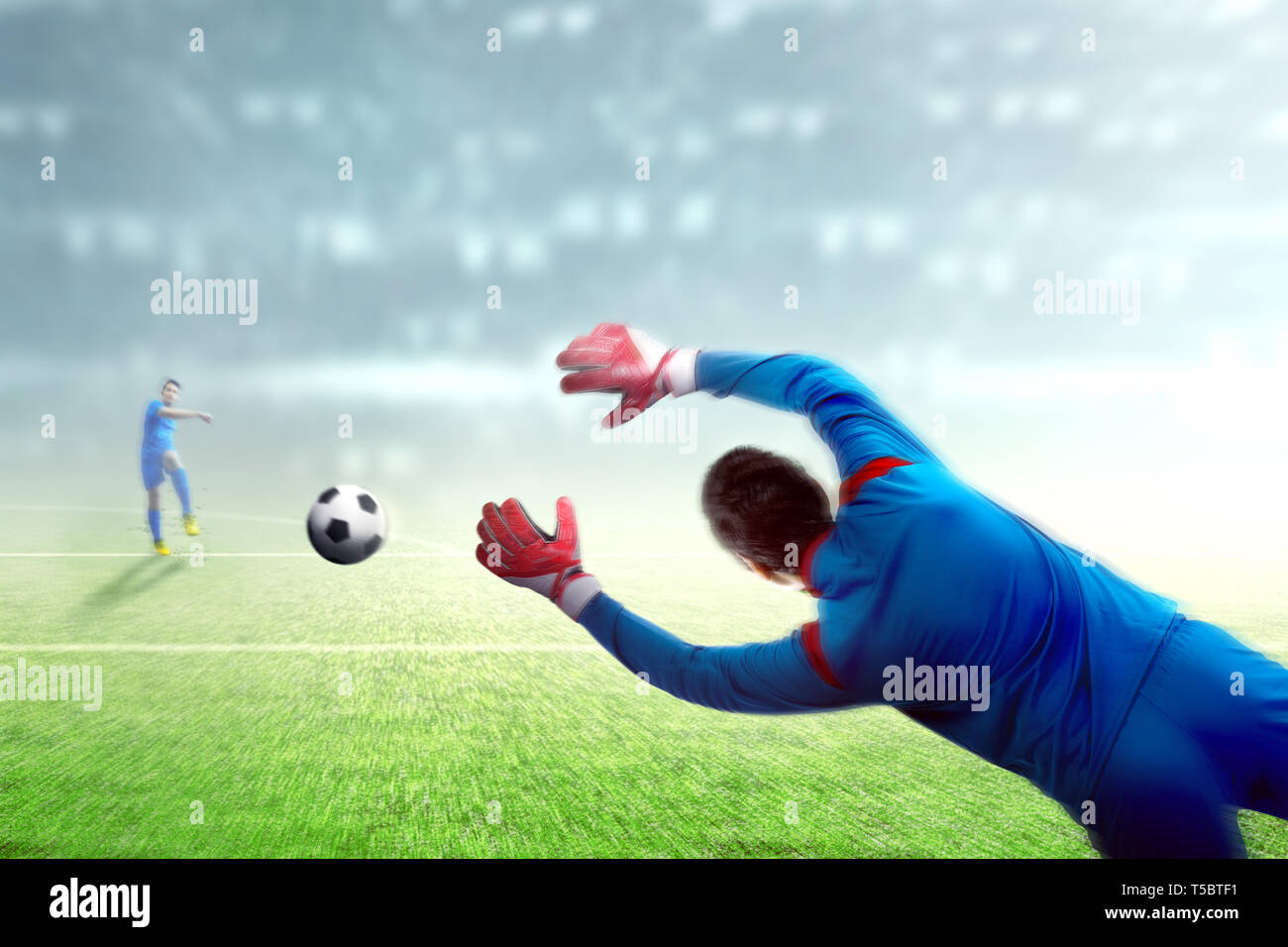 Asian giocatore di football uomo calciare la palla al traguardo su di un campo da calcio a Stadium Foto Stock