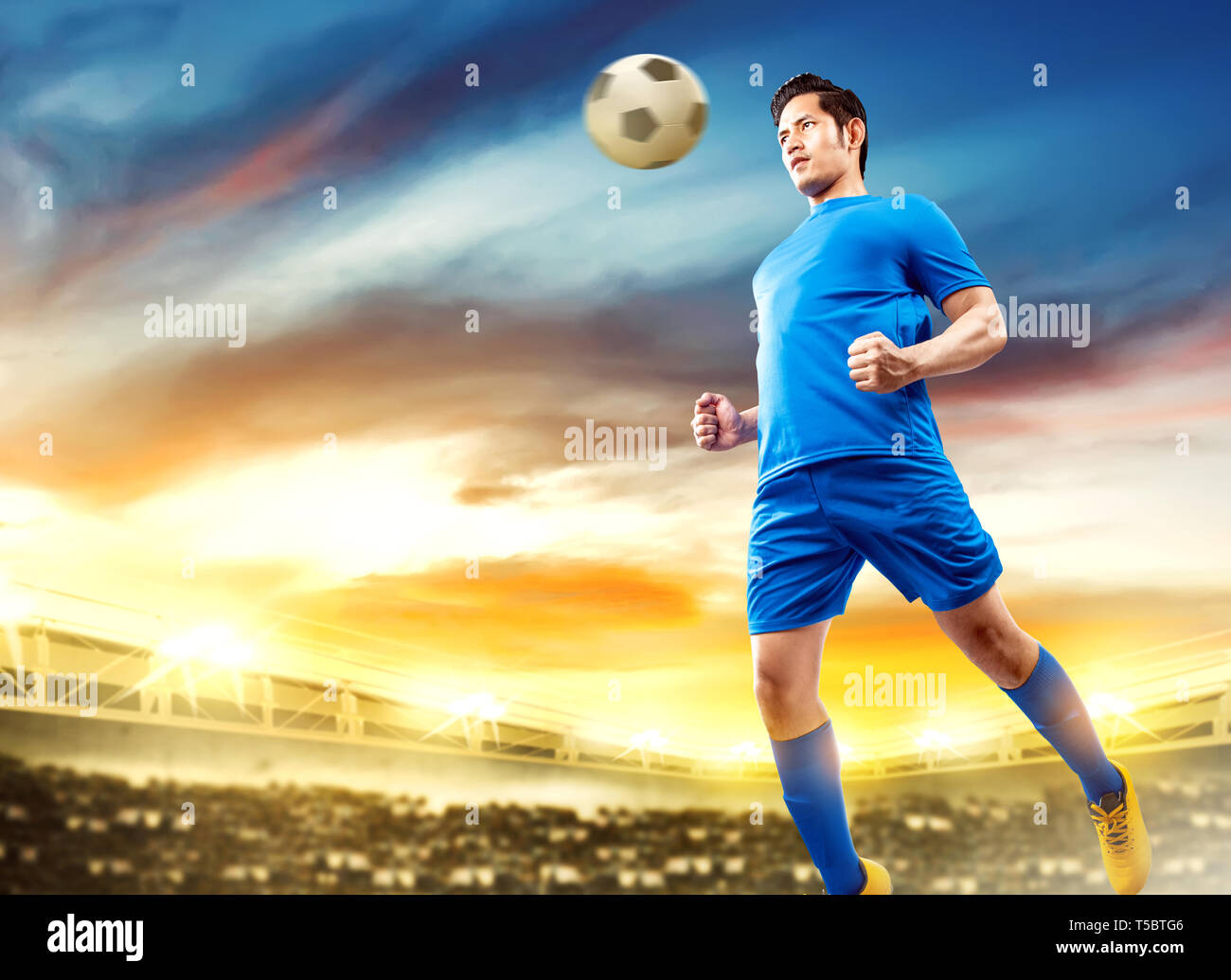 Asian giocatore di football uomo saltare in aria e la voce la palla sul campo di calcio a Stadium Foto Stock