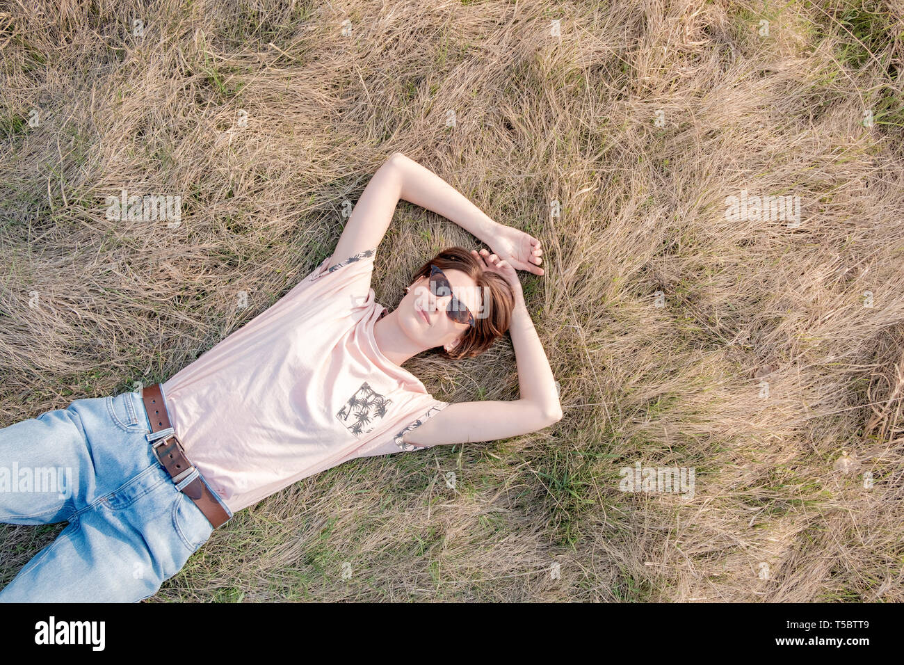 Giovane donna sull'erba apprezza la molla. Vista dall'alto di una rilassata persona di sesso femminile che stabilisce nel prato o un campo guardando il cielo Foto Stock