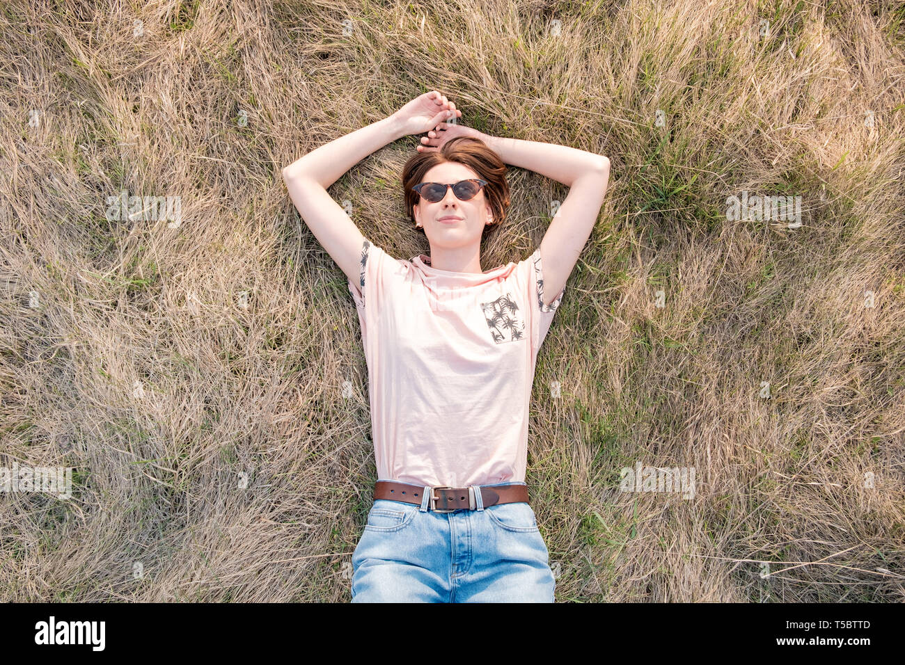 Giovane donna sull'erba godendo la molla. Vista dall'alto di un sorridente persona di sesso femminile che stabilisce nel prato o un campo guardando il cielo Foto Stock