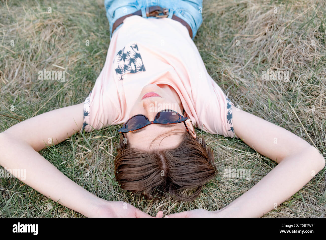 Giovane donna si appoggia sull'erba godendo la molla. Vista dall'alto di un sorridente persona di sesso femminile che stabilisce nel prato o un campo guardando il cielo Foto Stock