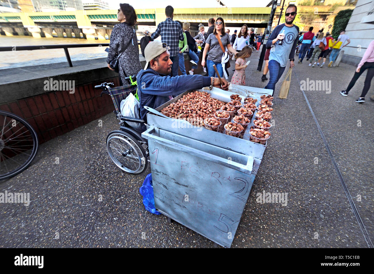 Londra, Inghilterra, Regno Unito. Uomo in sedia a rotelle vendita dadi caramellato sulla South Bank, Southwark Foto Stock