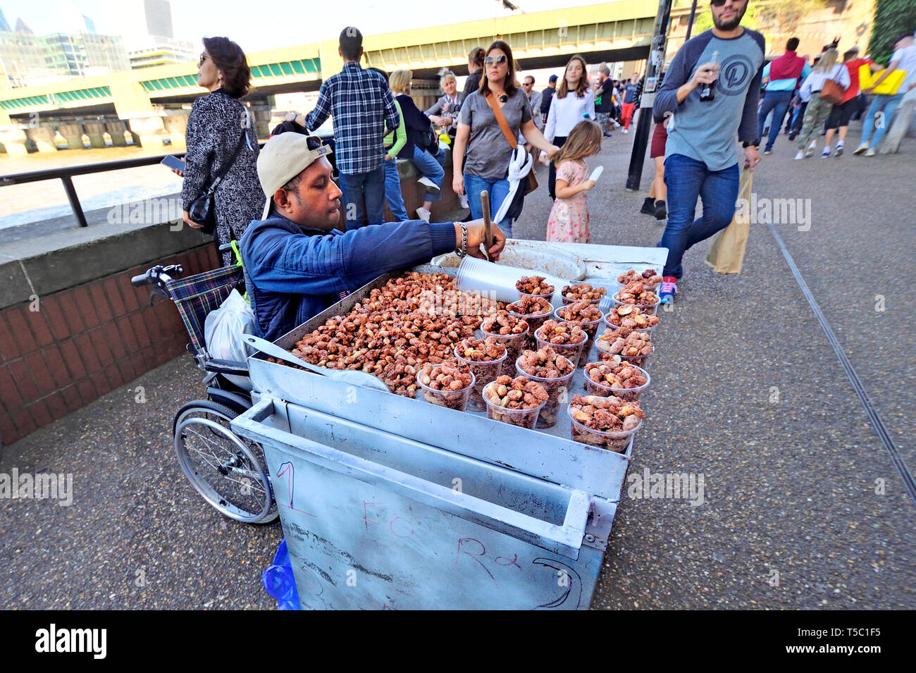 Londra, Inghilterra, Regno Unito. Uomo in sedia a rotelle vendita dadi caramellato sulla South Bank, Southwark Foto Stock