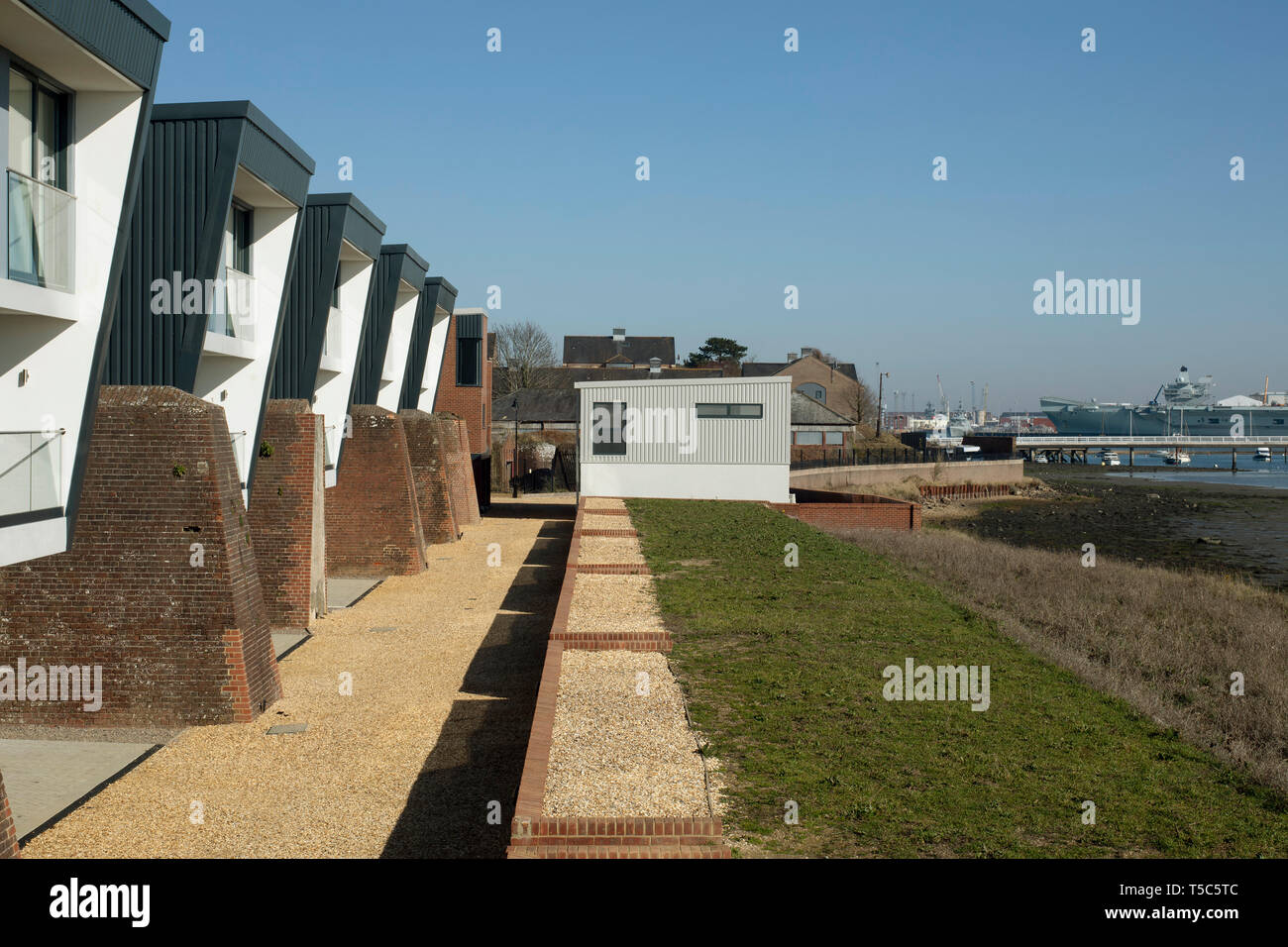 Vista guardando lungo la fila di case con nave militare in background. Priddys Hard, Gosport, Regno Unito. Architetto: John Pardey architetti, 2019. Foto Stock
