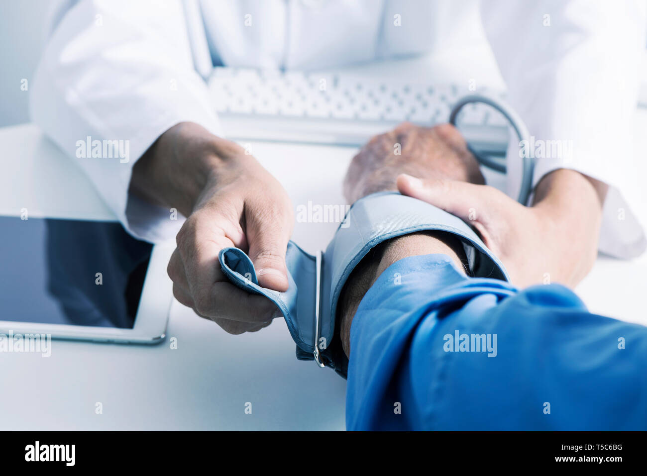 Primo piano di un medico caucasica uomo in camice bianco, circa per misurare la pressione del sangue di un senior caucasica uomo paziente con uno sfigmomanometro, sit Foto Stock