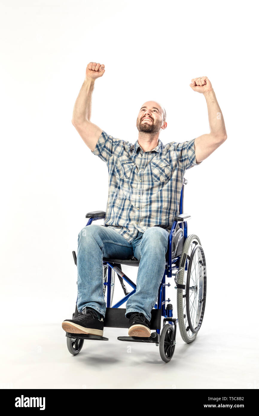 Uomo in sedia a rotelle sorridente e a braccia alzate in segno di vittoria. Concetto di disabilità e il pensiero positivo. Foto Stock
