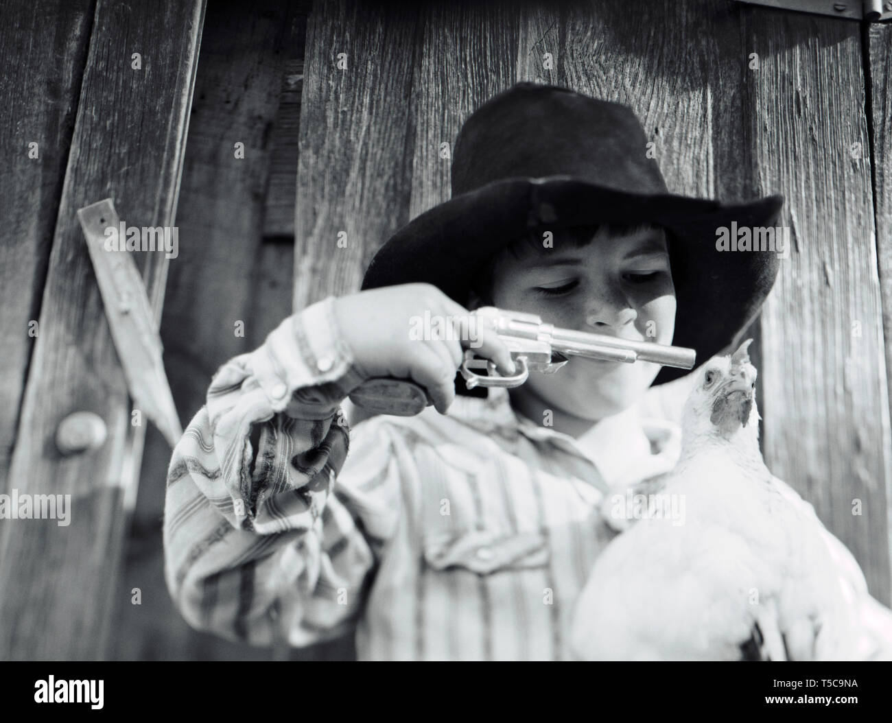 Ragazzo che indossa un cappello e puntando una pistola giocattolo a un pollo  alla testa Foto stock - Alamy