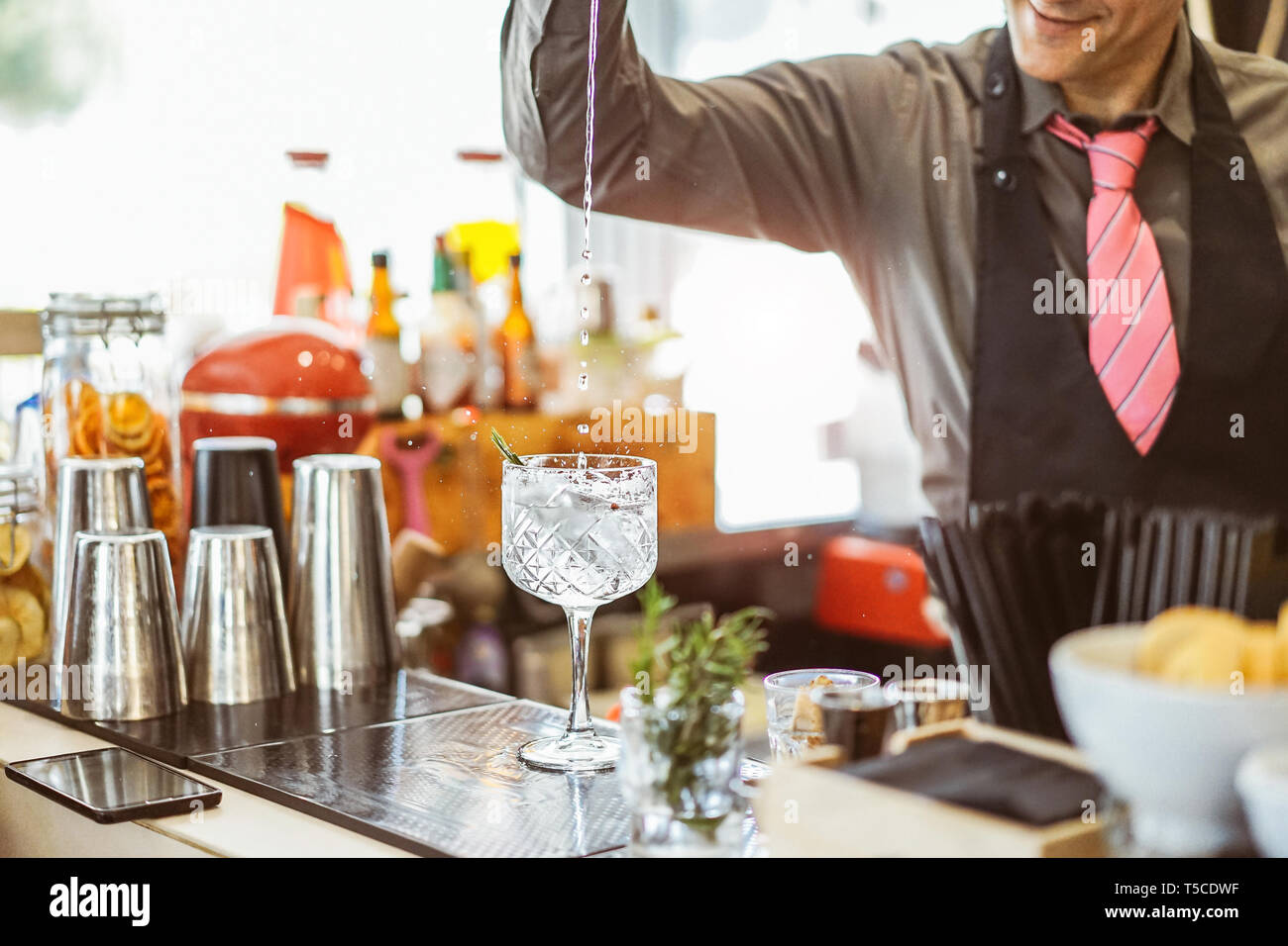 Barista miscelare un cocktail in un bicchiere di cristallo in un american bar - il barman versando alcool in un bicchiere con erbe aromatiche Foto Stock