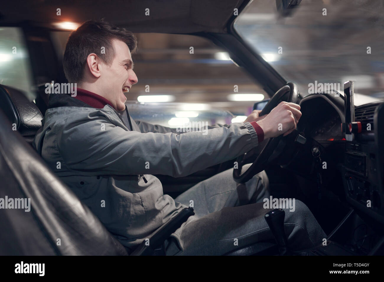 Foto dal lato del giovane maschio urlando conducente seduto in auto Foto Stock