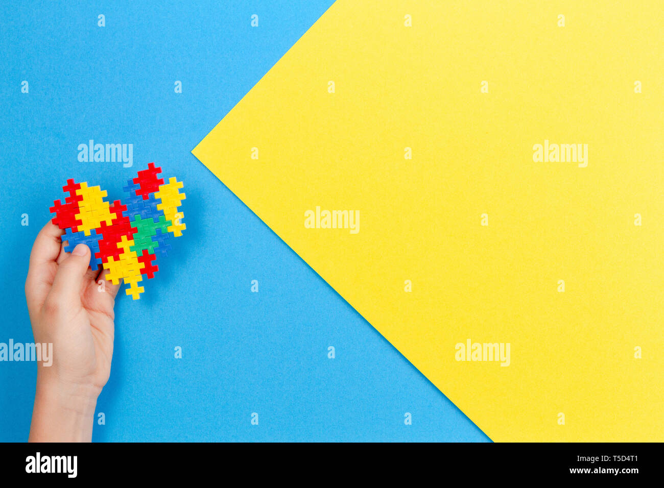 Bambino mano azienda cuore colorati in giallo e blu sullo sfondo. Mondo autismo consapevolezza giorno di concetto Foto Stock