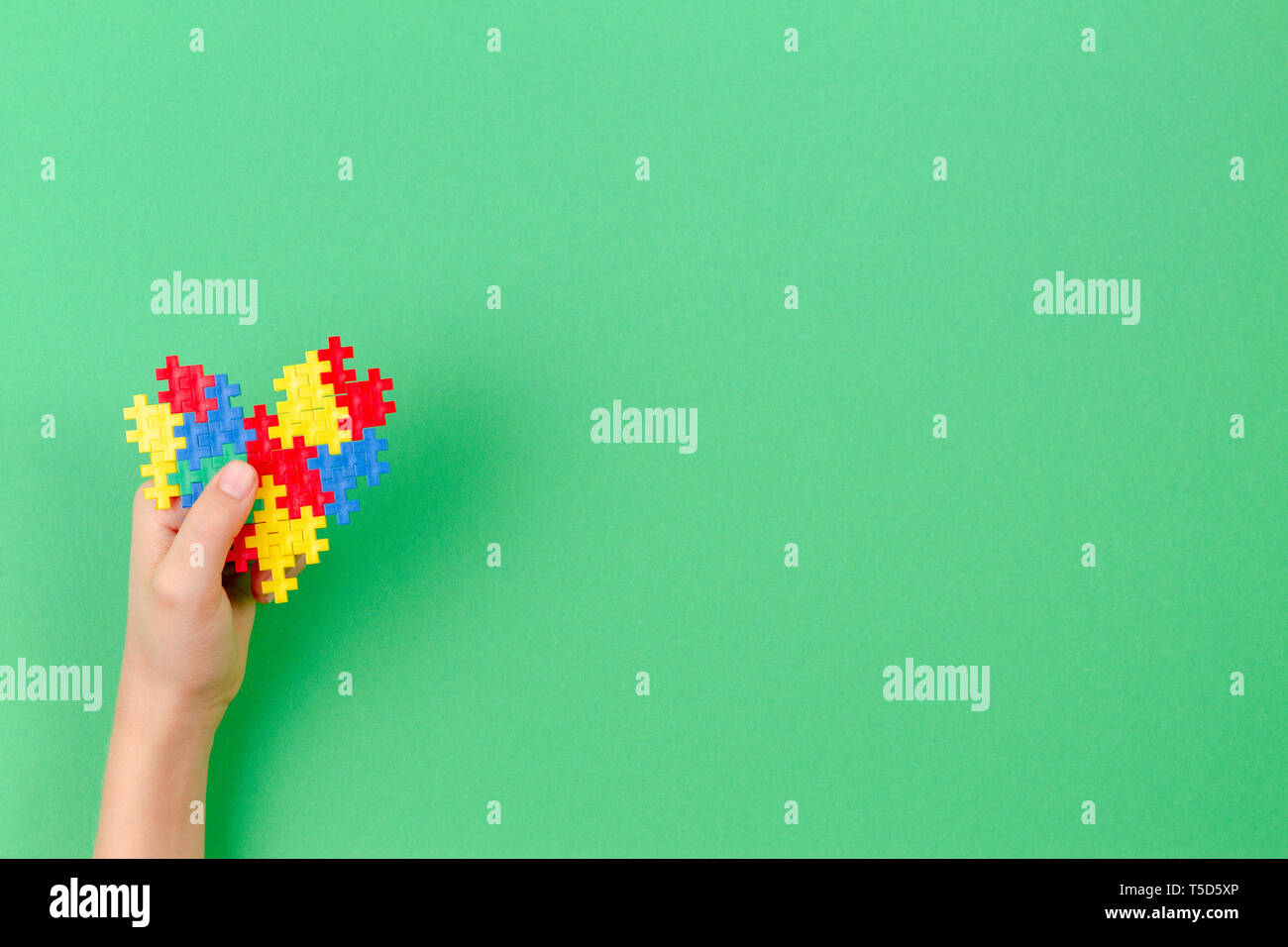 Bambino mano azienda cuore colorati su sfondo verde. Mondo autismo consapevolezza giorno di concetto Foto Stock