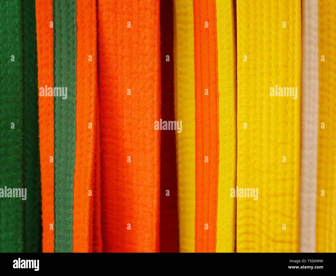 Primo piano di arti marziali cinghie per il karate o kickboxing - bianco con cartellino giallo, giallo, giallo con etichetta arancione, arancione, arancione con etichetta verde, verde Foto Stock