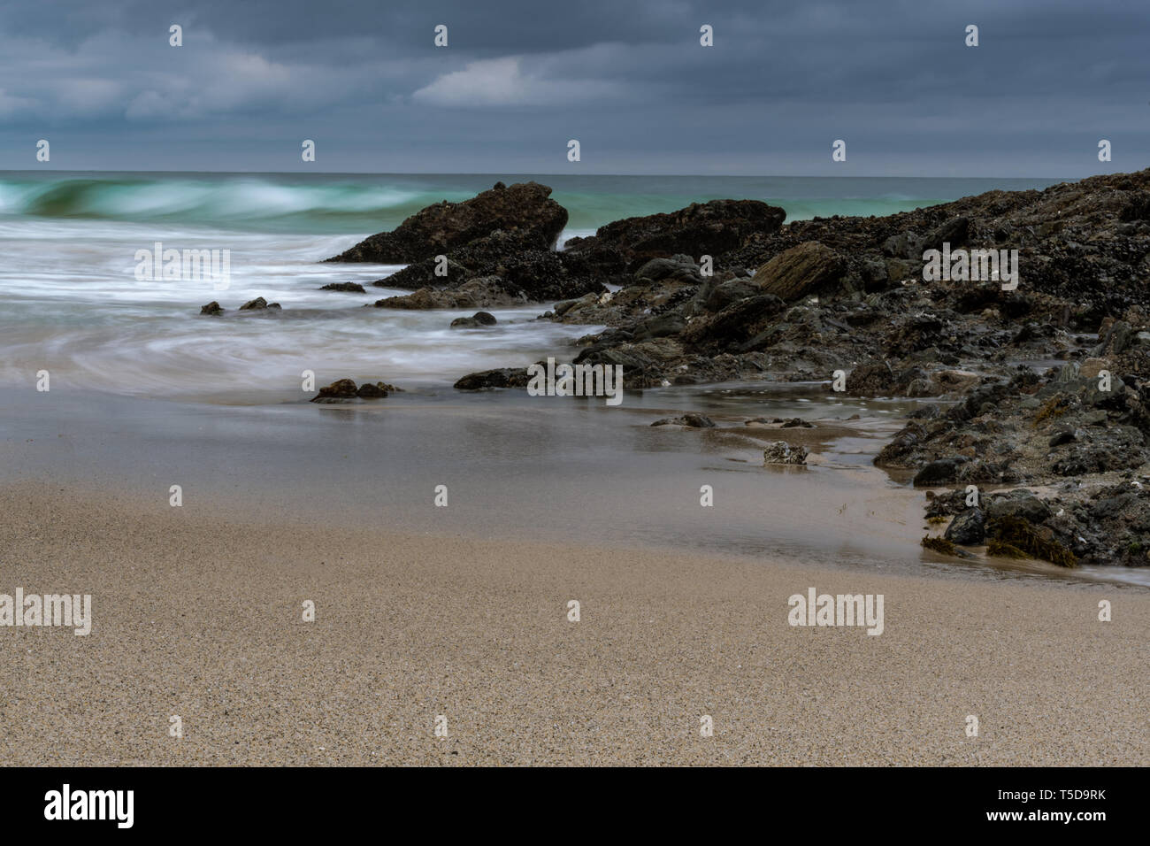 Una spiaggia tranquilla scena ripresa durante l'alba con liscia e setosa drifting onde attraverso la sabbia e rocce. Una lunga esposizione bellissima alba sulla costa. Foto Stock