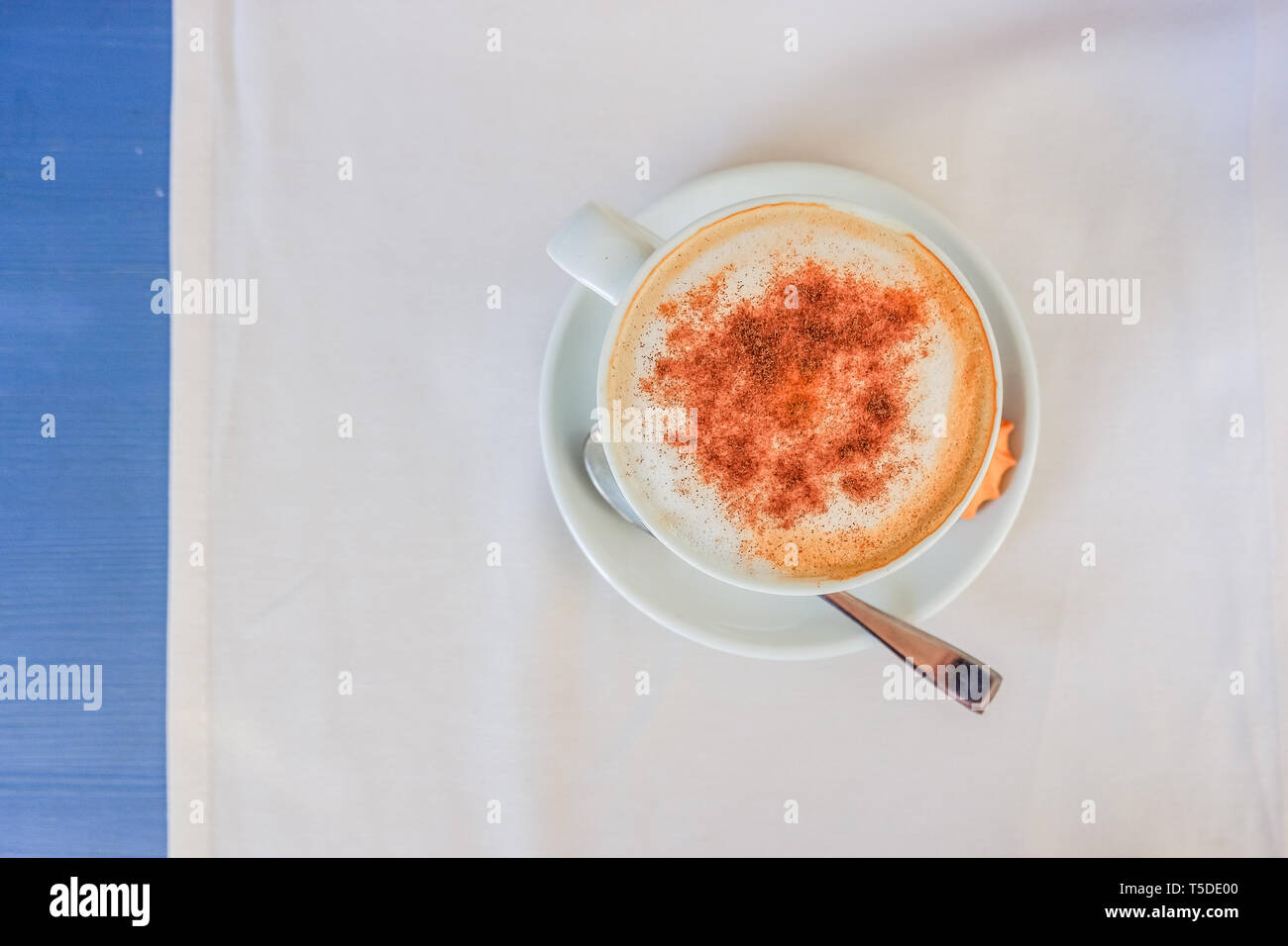 White tazza di cappuccino con cannella sulla luce tavolo blu con tovagliolo bianco, vista dall'alto. Buon Caffè la mattina. Buon umore per tutto il giorno bevande calde Foto Stock
