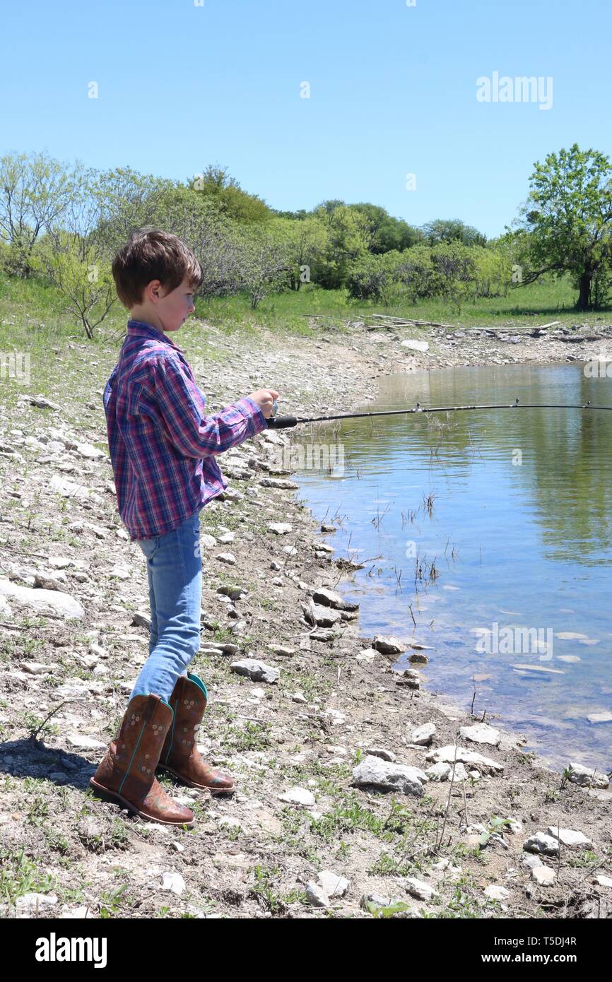 Bambino con breve marrone capelli e stivali da cowboy di pesca sul bordo di  un lago Foto stock - Alamy