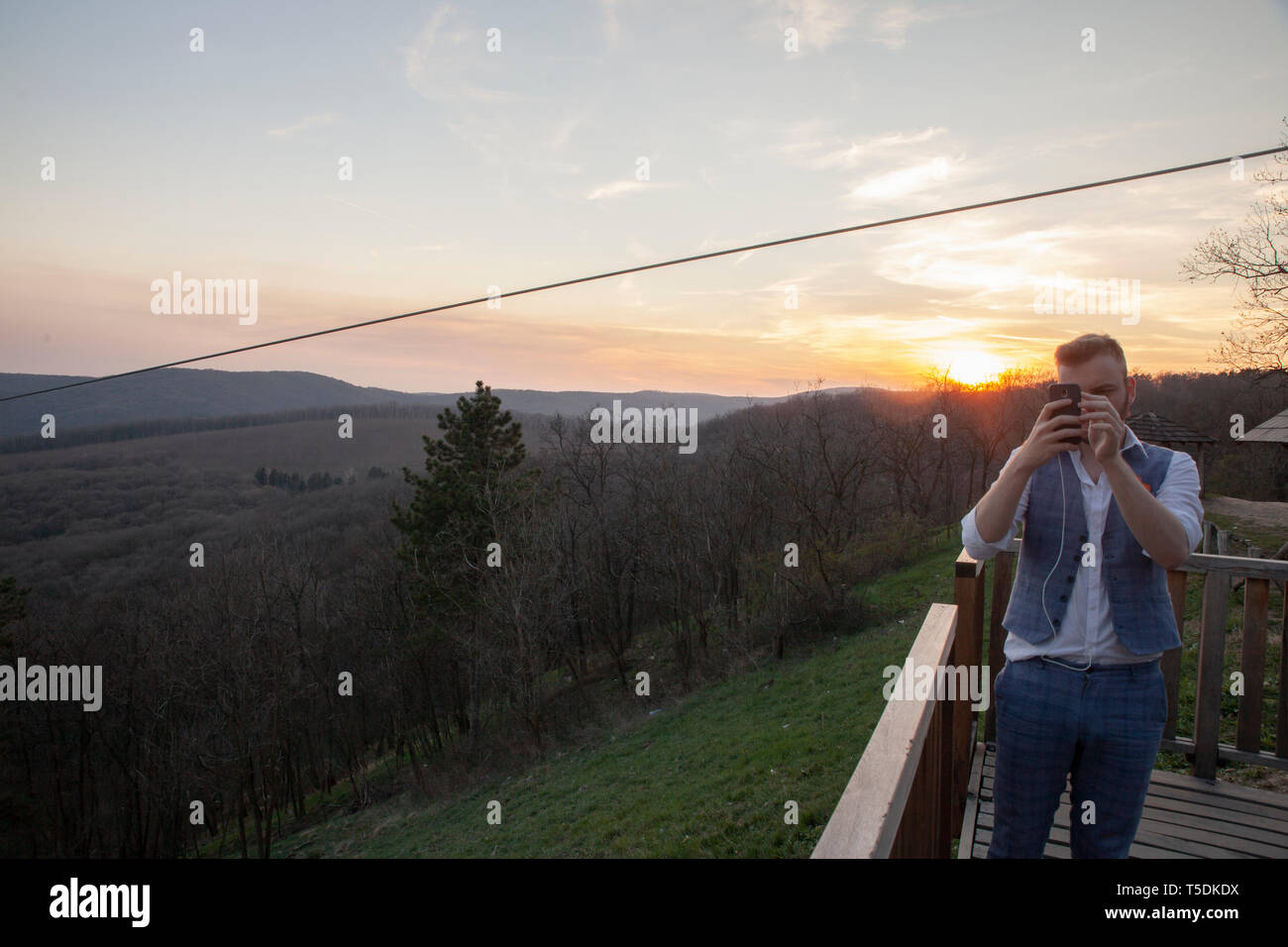 Candid shot, turistico di fronte a una telecamera, parlando di una foto sul suo telefono cellulare, sulla montagna. In fondo è il tramonto della gamma della montagna e del cielo. Foto Stock