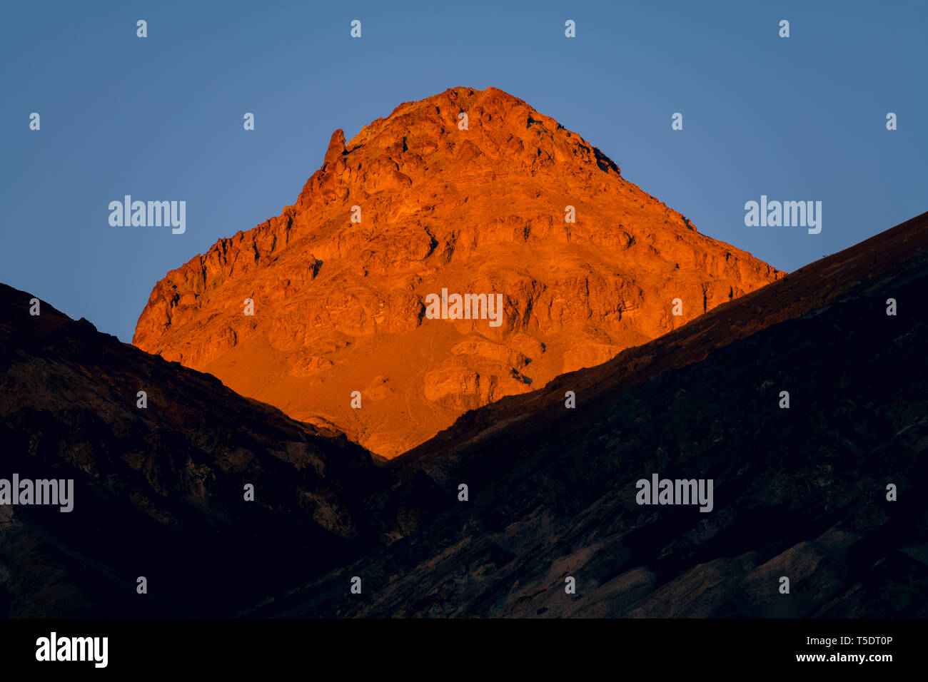 Alto picco di deserto illuminato dalla luce dorata del tramonto sopra una cresta che è in ombra - Parco Nazionale della Valle della Morte Foto Stock