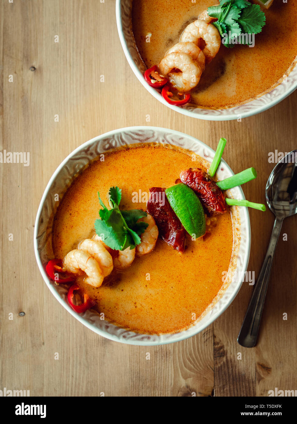 Tom Yam kong pronto a mangiare. Tom Yum Zuppa di gamberetti su un tavolo di legno. Speziato popolare piatto tailandese Tom Yam vista dall'alto. Thailandia il cibo e la cucina tailandese. Verticale. La luce naturale del giorno Foto Stock