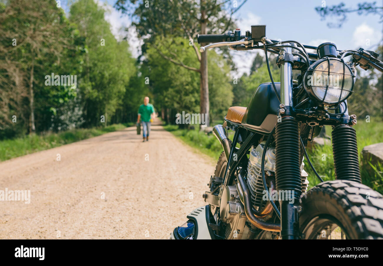Custom vintage moto sul lato della strada con guy in background a piedi con benzina può Foto Stock