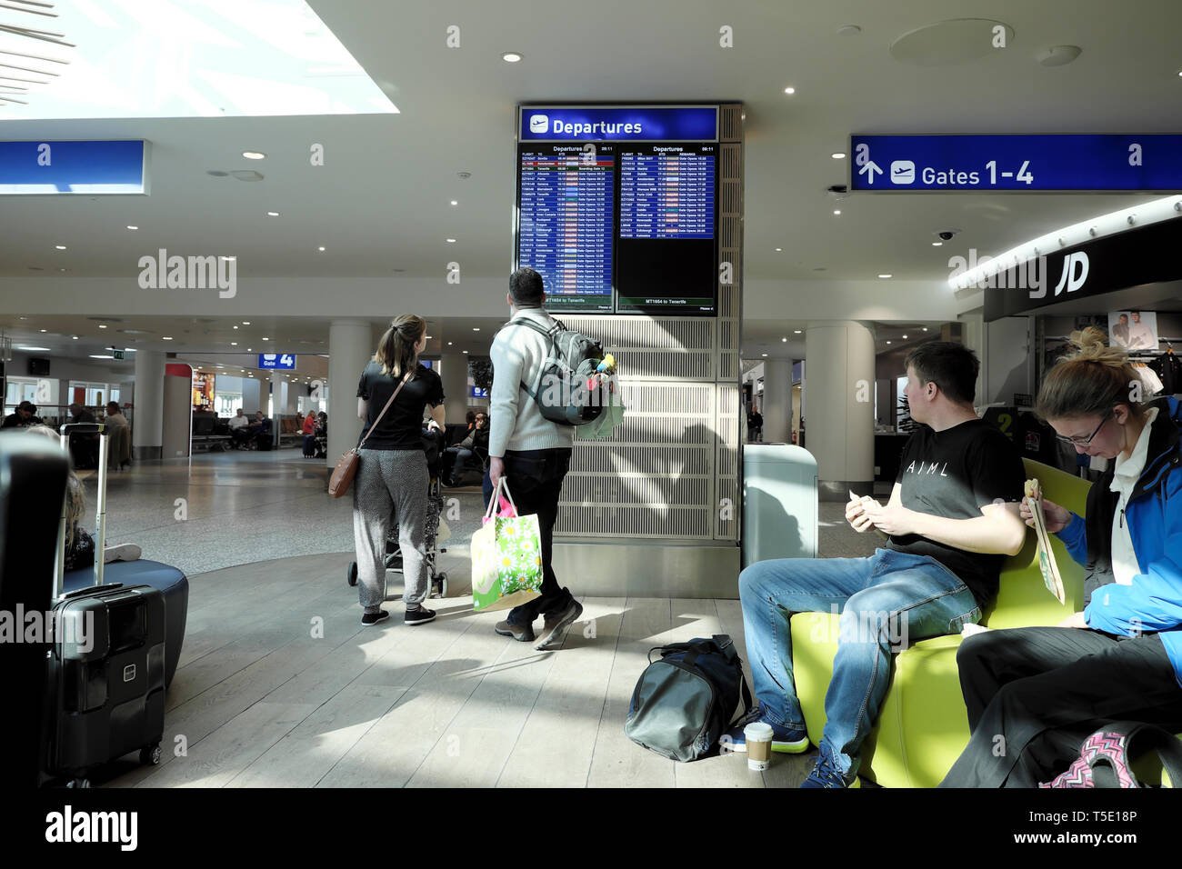 I passeggeri in attesa di viaggiatori alla ricerca di volo a partenze elettronico display & seduta in Bristol Airport con sacchetti per andare in vacanza in Europa 2019 Foto Stock