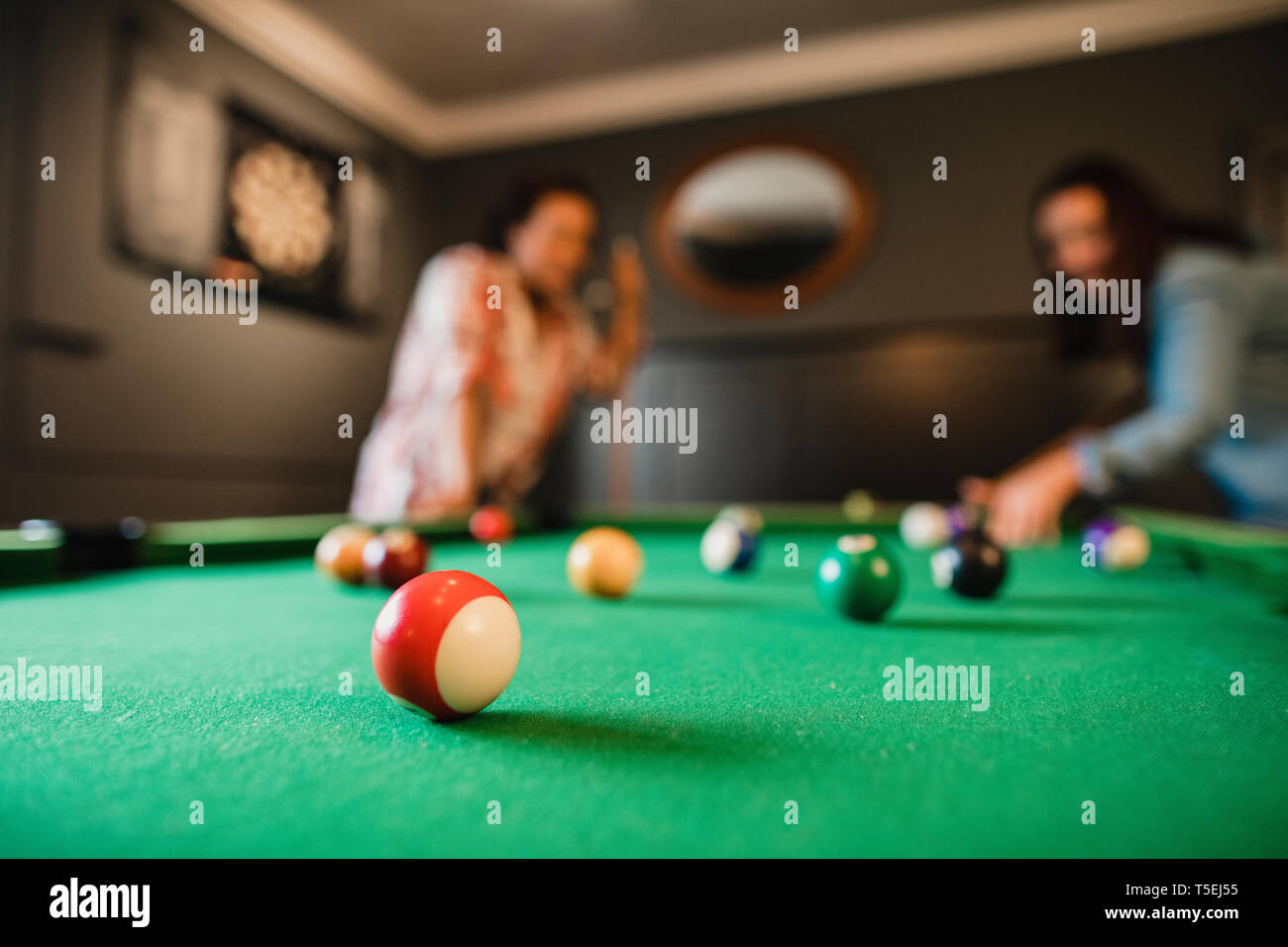 Focus sul primo piano di un rosso striato palla in piscina. Sullo sfondo vi sono due metà amici adulti giocando una partita a biliardo nella sala giochi in una casa. Foto Stock